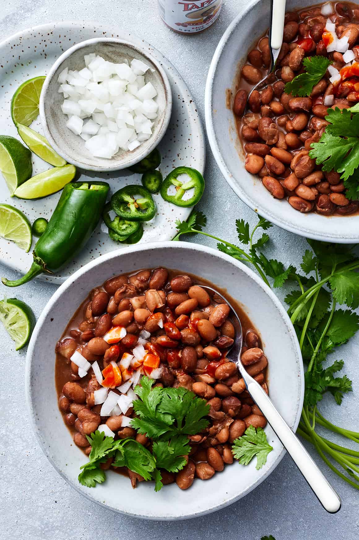 Instant Pot pinto beans in bowls with cilantro, onion, and hot sauce