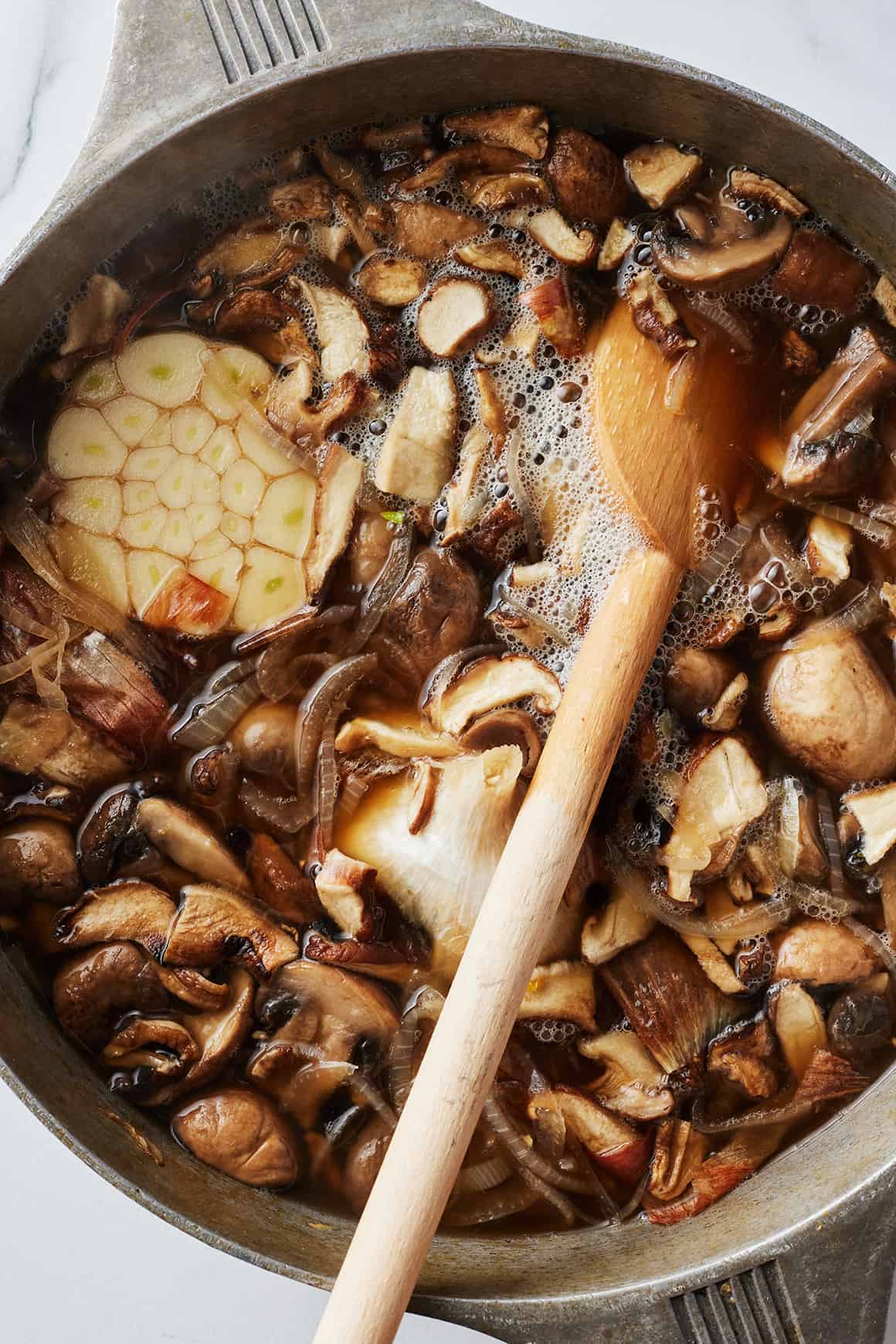 Simmering mushroom broth in pot with wooden spoon